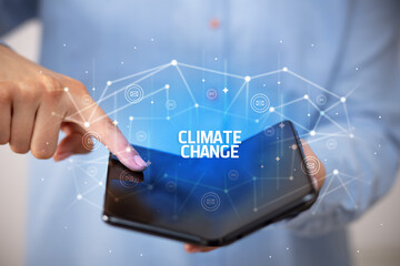 Businessman holding a foldable smartphone with CLIMATE CHANGE inscription, new technology concept