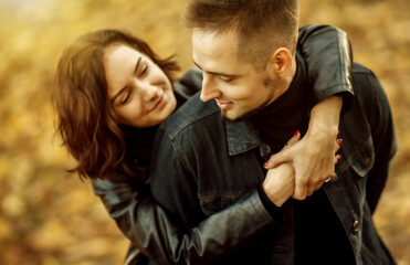 Portrait of a young hugging couple of lovers on a blurry background of fallen autumn leaves in the park.