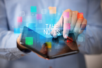 Young man holding a foldable smartphone with TAKE NOTES inscription, educational concept