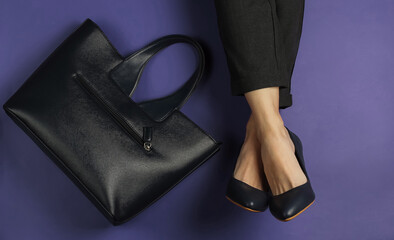 Female legs dressed in trousers and classic shoes with heels and bag on purple background. Top view. Beauty and fashion studio shot