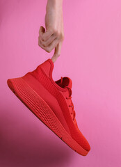 The hand holds red sports shoe on pink background. Studio shot