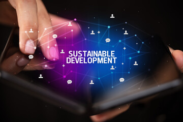 Businessman holding a foldable smartphone with SUSTAINABLE DEVELOPMENT inscription, new technology concept
