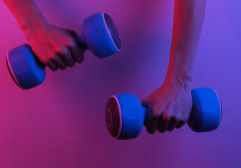 Female hands hold dumbbells. Creative pop art pink blue neon color. Trendy gradient illumination. Night light