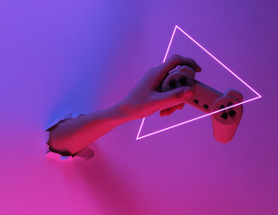 Hand holds gamepad through torn hole. Creative pop art pink blue neon color. Trendy gradient illumination. Night light © splitov27
