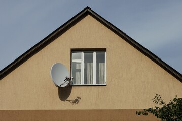 brown loft of a private house with one window and a white satellite dish outside against a blue sky