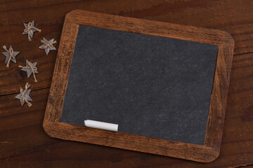 A vintage blank slate chalkboard with wood holdiay stars on a rustic wood surface.