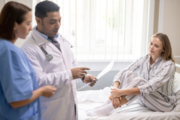 Young woman sitting on bed and looking at confident doctor pointing at paper