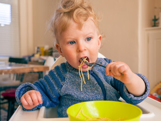 One year old baby boy eating spaghetti with cutlery at home