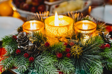 Fototapeta na wymiar Beautiful new year's holiday candle holder with three candles and lights among green spruce branches and red frosty berries with Golden cones. Warm and cosy decoration