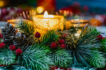 Obraz na płótnie Canvas Beautiful new year's holiday candle holder with three candles and lights among green spruce branches and red frosty berries with Golden cones. Warm and cosy decoration
