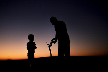 The silhouette of a young boy and an adult man in the desert sunset