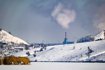 High and wide chimney, a pipe with a large amount of smoke and substances released into the atmosphere. Part of a factory or enterprise that pollutes the environment in a snowy and frosty winter near 