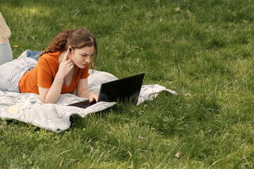 Naklejka na ściany i meble Close up portrait of upset girl college student lying on the green grass with laptop and wireless headphones. Woman see bad news in the internet and feel bad. Image with text copy space.