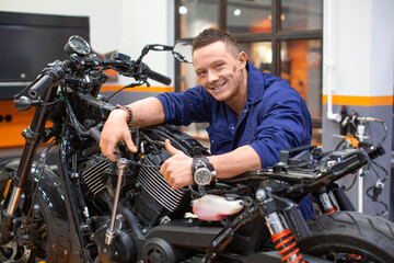 Fototapeta na wymiar Smiling man in a repair shop near a motorcycle shows thumbs up.
