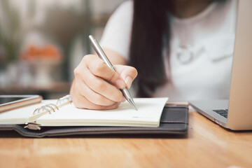 Fototapeta premium Closeup of woman's hand holding a pen on notebook. Freelance journalist working at home.