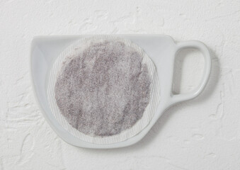 Black tea tea bag on ceramic plate with cup shape on light.