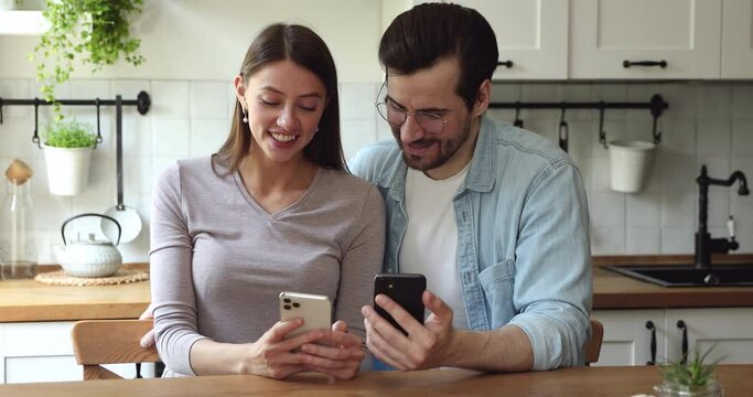 Addicted to technology young married couple holding smartphones in hands, sharing funny video photo content or useful software application, spending free leisure time discussing online media news.