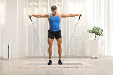 Full length hot of a muscular guy exercising with a resistance band at home