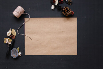 flat lay of brown paper with space for text on a dark surface with pine cones and pout pourry