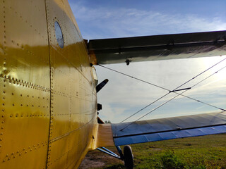 Yellow and blue old biplane plane with a single piston engine and propeller against a blue sky with clouds on the airfield with green grass in summer
