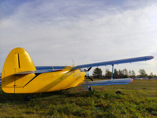 Yellow and blue old biplane plane with a single piston engine and propeller against a blue sky with clouds on the airfield with green grass in summer