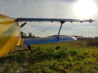 Yellow and blue old biplane plane with a single piston engine and propeller against a blue sky with clouds on the airfield with green grass in summer