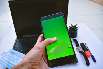Overhead view of businesswoman hand tapping on green screen mobile phone. Blur laptop computer on office table