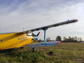 Yellow and blue old biplane plane with a single piston engine and propeller against a blue sky with clouds on the airfield with green grass in summer
