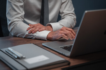 Fototapeta premium Businessman in white shirt and gray tie in front of a laptop on a wooden desk with items