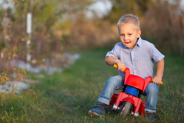 A little boy on a red motorcycle rides on the green grass.
