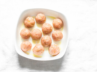 Raw chicken meatballs in a baking dish on a grey background, top view. Cooking baked meatballs