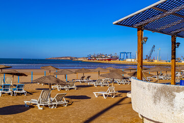 Deserted beach with umbrellas and chairs,and the harbor with colorful fishing boats in Essaouria, Morocco.North Africa.