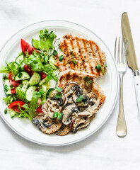 Balanced food - grilled turkey with creamy mushroom sauce and fresh vegetable salad on a light background, top view