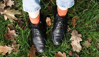 Female legs in black boots on green grass with yellow fallen autumn leaves in the park. Autumn...