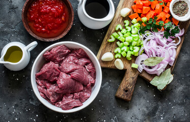 Ingredients for cooking beef in burgundy - beef fillet, tomato sauce, red wine, vegetables on a dark background, top view