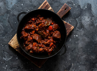 Burgundy beef stew in a pan on a dark background, top view. Delicious comfortable homemade food