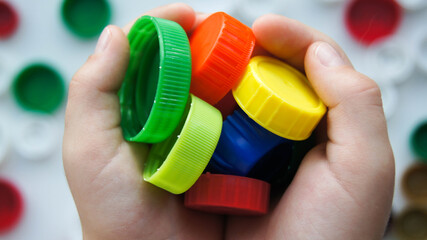 Childs hands holding colourful plastic bottles caps for recycling to conserve the environment....