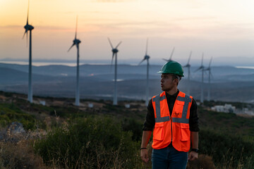 Young maintenance engineer working in wind turbine farm at sunset