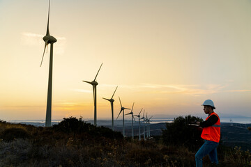 Fototapeta na wymiar Young maintenance engineer working in wind turbine farm at sunset