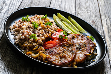 Roasted meat, buckwheat and pickled cucumbers on wooden table
