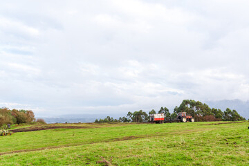 Naklejka premium red agricultural tractor standing in a meadow on top of a hill. rural and environment concept
