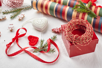 Christmas background with gift boxes, ribbon, twine, paper rolls, knitted hearts and Christmas ornament.