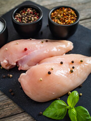 Fresh raw chicken fillet on cutting board with spices on wooden table
