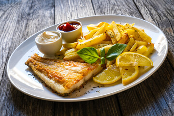 Fish dish - fried cod fillet with French fries and vegetable salad on wooden table
