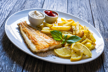 Fish dish - fried cod fillet with French fries and vegetable salad on wooden table
