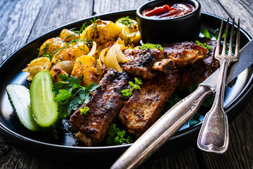 Tasty roasted ribs with baked potatoes vegetables on wooden table