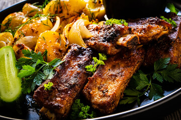 Tasty roasted ribs with baked potatoes vegetables on wooden table