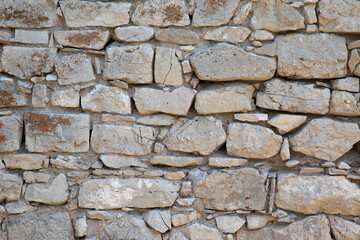 Stone wall. Consists of individual small stone blocks covered with moss. Great gray background.