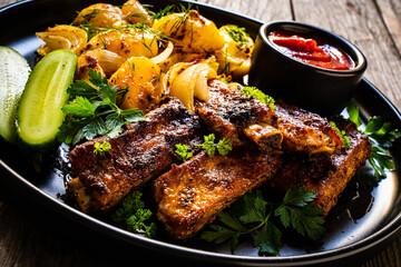 Tasty roasted ribs with baked potatoes vegetables on wooden table
