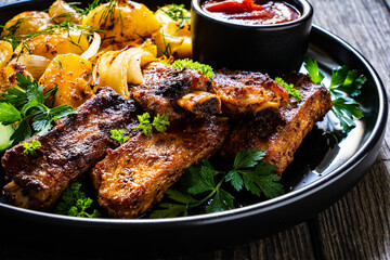 Tasty roasted ribs with baked potatoes vegetables on wooden table
